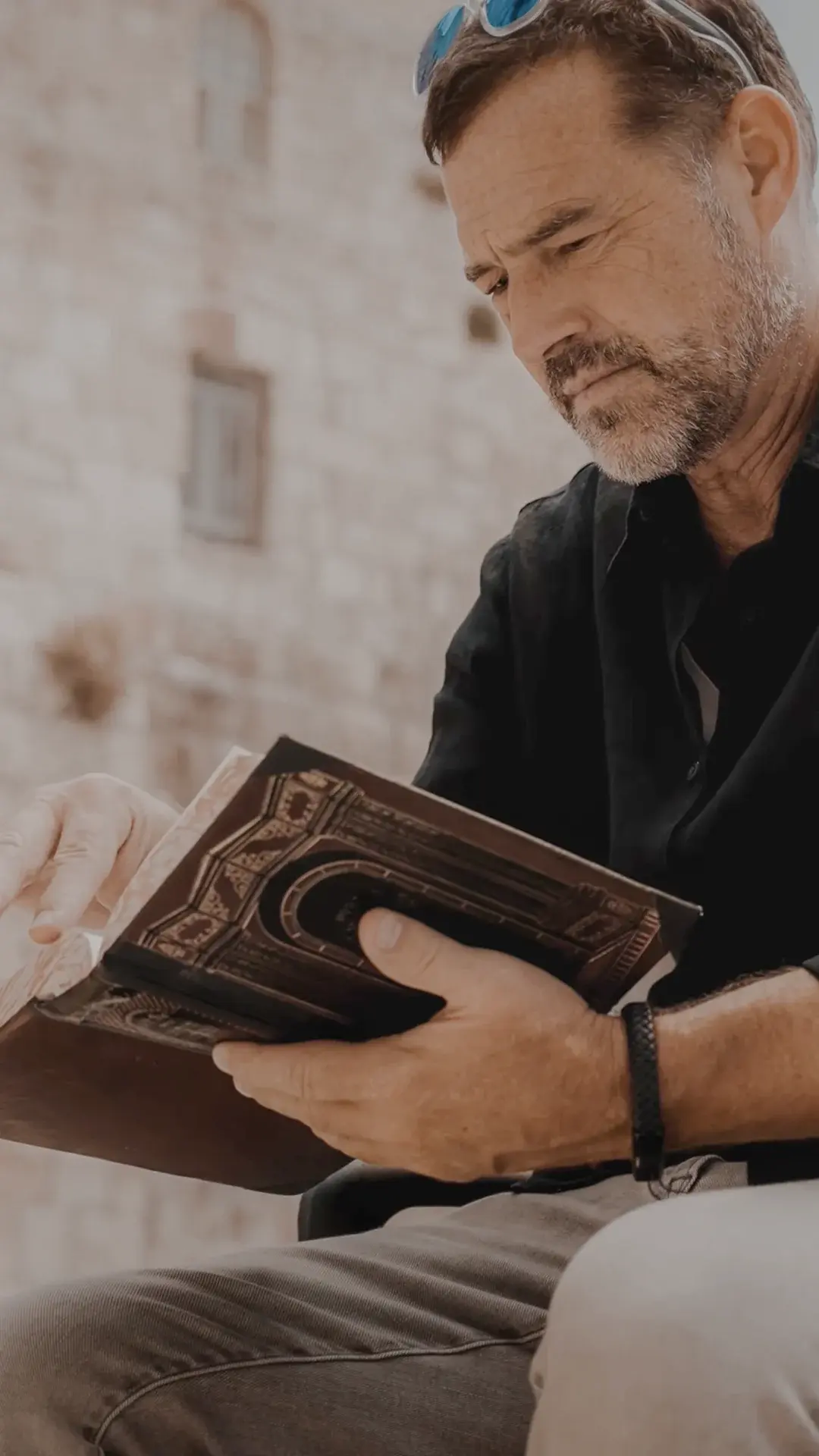 A man sits in front of the Western Wall in Jerusalem, reading the Bible.