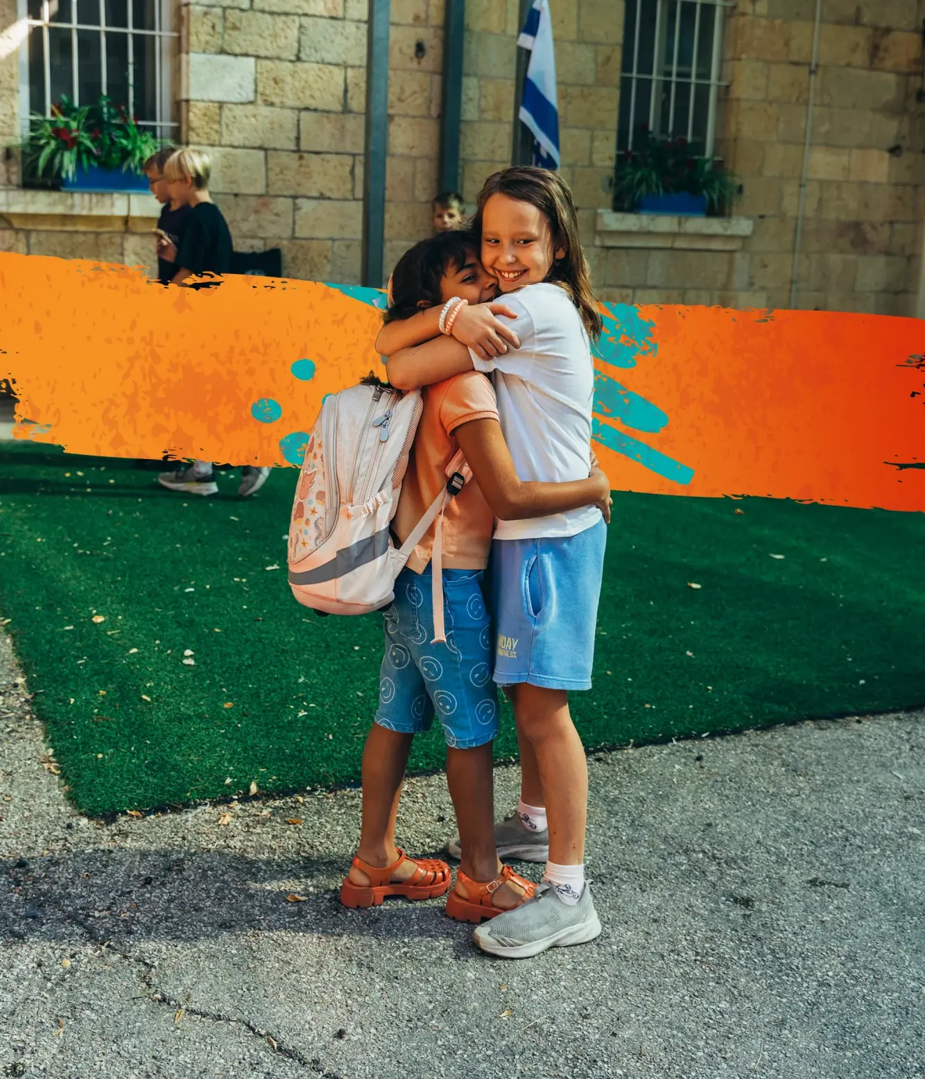 Two gradeschool girls hug on a playground with huge smiles on their faces.