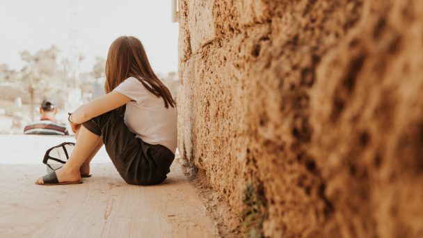 girl sitting against a rock wall