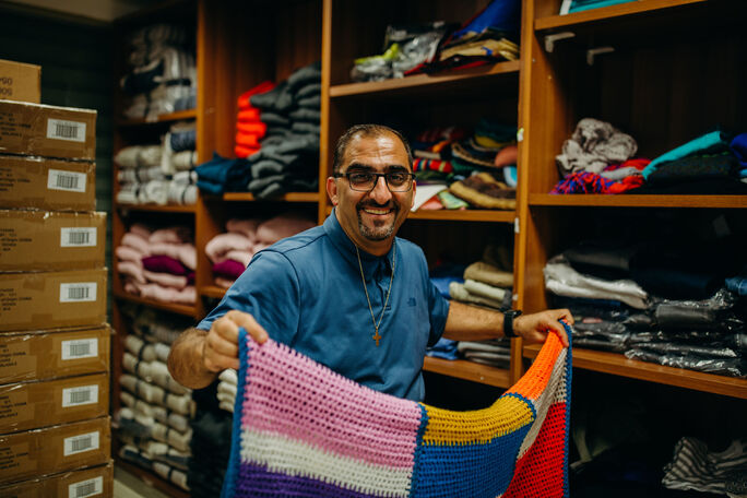 man showing off a colorful knitted blanket
