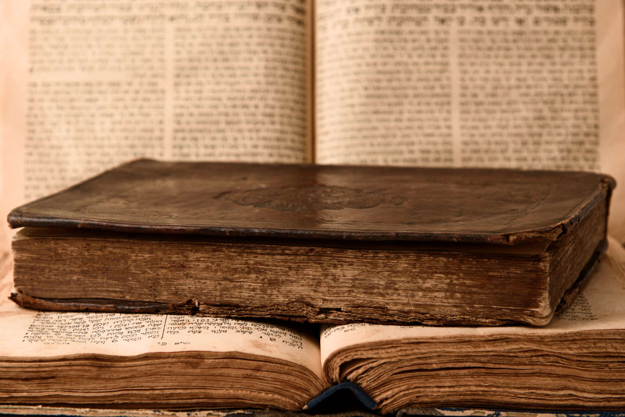 Old worn shabby jewish books in leather binding and open blurred Torah in the background. Closeup. Selective focus.