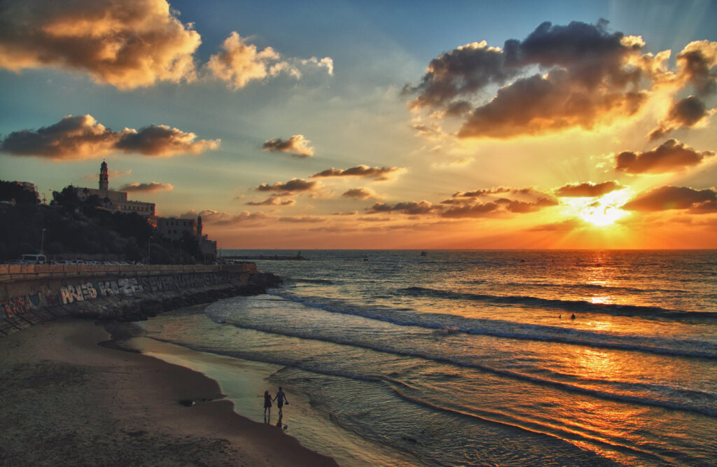 TEL AVIV, ISRAEL - June 11, 2013 : A sihluette of young couple walking on the beach on background of sunset scenery of old Jaffo promenade in Tel Aviv, Israel.