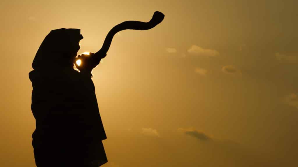 Jewish man blowing shofar in the sunrise