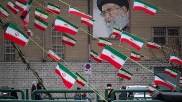 An Iranian cleric walks under a portrait of Irans Supreme Leader